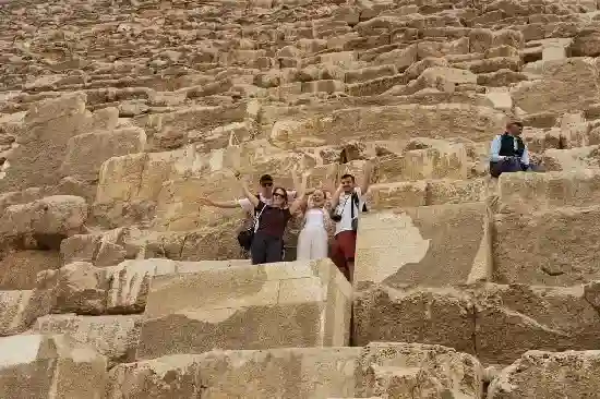 A couple hugging in front of the pyramids and tourists exploring the ancient stones.