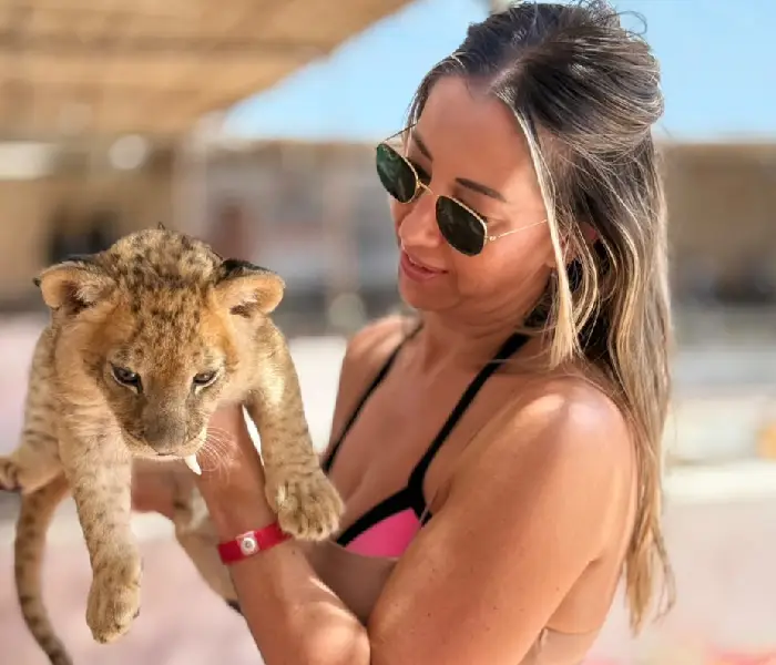 Woman wearing sunglasses holding a small baby lion cub in Hurghada